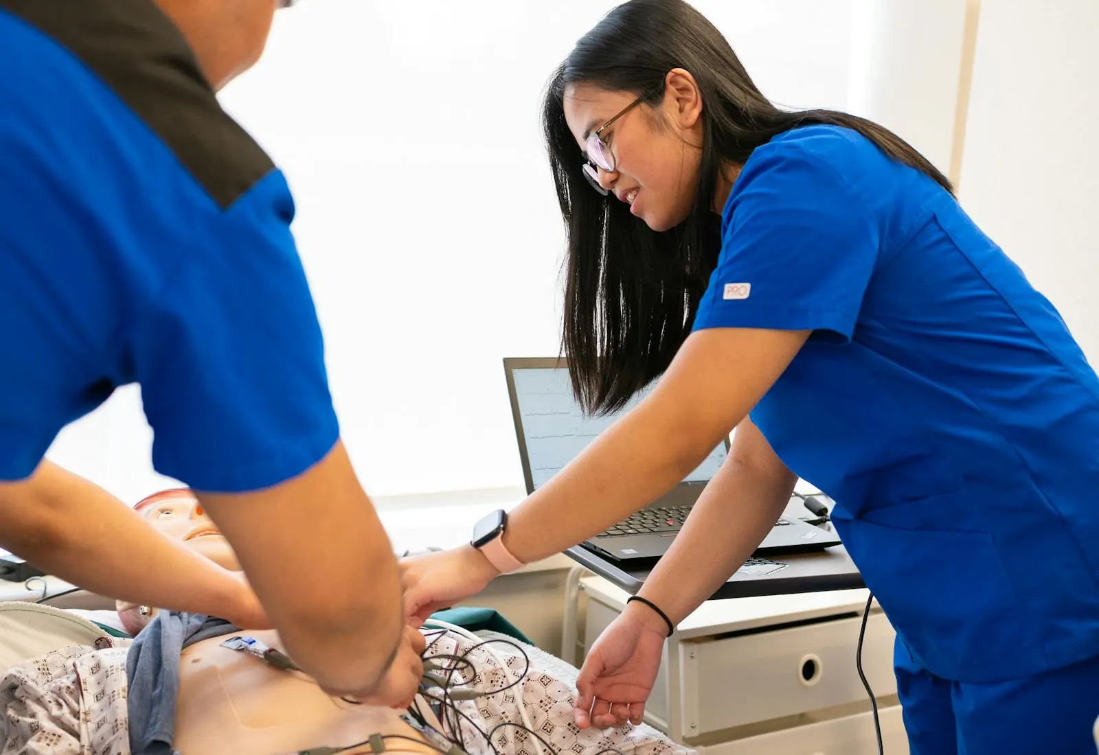 Two nursing students reviewing simulation data on a laptop beside a training mannequin.